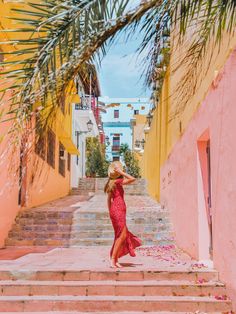 a woman in a red dress is walking down some stairs with palm trees on either side