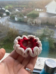 a hand holding a small red and white object in front of a window with a view of houses