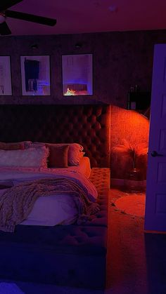 a large bed sitting in a bedroom next to a purple lit room with pictures on the wall