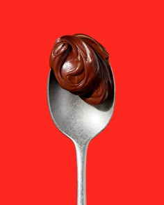 a spoon filled with chocolate frosting on top of a red background