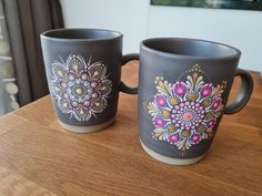 two coffee mugs sitting on top of a wooden table next to each other with designs painted on them