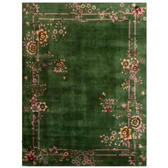 a green area rug with flowers and vines on the border, in front of a white background