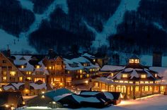 a large building surrounded by snow covered mountains at night with lights on the buildings and trees in the background