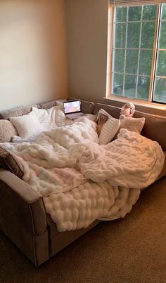 an unmade bed in the corner of a room with a laptop on top of it