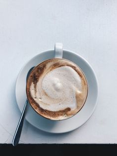 a white plate topped with a cup of coffee next to a spoon on top of a table