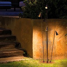 two lamps on the side of a wall next to some grass and stairs at night