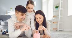 a man and woman playing with a piggy bank on the floor in their living room