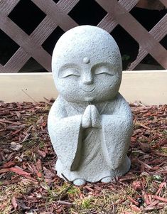 a statue of a buddha sitting on top of some mulch next to a fence