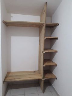 an empty closet with wooden shelves and tile flooring on the walls, in front of a white wall