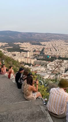 people are sitting on the edge of a hill looking out at the city below them