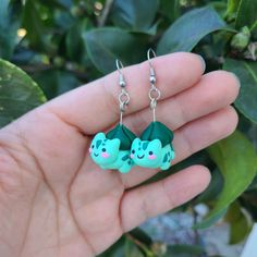 a pair of green earrings with cats on them sitting in front of a leafy tree