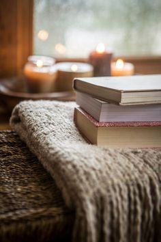 a stack of books sitting on top of a wooden table next to a candle holder