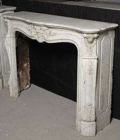 a white fireplace with an ornate design on the top and bottom, next to a black wall