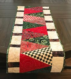 a table runner made with red, green and black quilted material on top of a wooden table