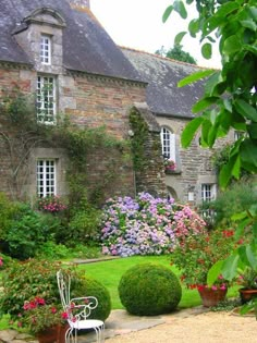 an old stone house with flowers in the front yard