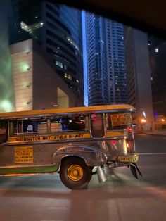 an old school bus driving down the street in front of some tall buildings at night