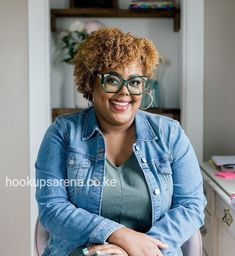 a woman sitting in a chair with her arms crossed and looking at the camera smiling