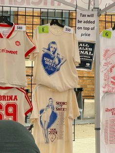 several t - shirts are hanging on a rack in front of a brick building with advertisements