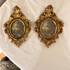 two gold framed pictures sitting on top of a white table cloth next to each other