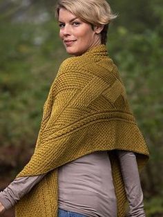 a woman wearing a yellow knitted shawl in front of some trees and bushes