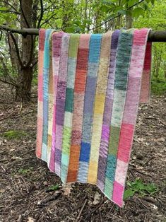 a multicolored quilt hanging from a tree in the woods