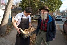 two men standing next to each other on a sidewalk with potatoes in front of them