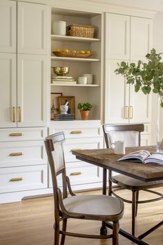 a dining room table with two chairs and a book on top of it in front of white cupboards