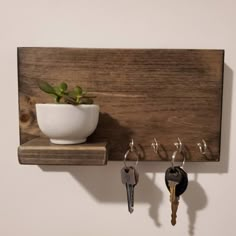 a wooden shelf with keys and a plant on it, hanging from the wall next to a white bowl