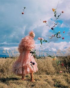 a woman standing in a field with flowers on her head and dress blowing in the wind