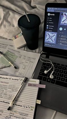 an open laptop computer sitting on top of a bed next to a cup and pen