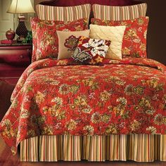 a red bed covered in lots of pillows next to a night stand with a lamp on it