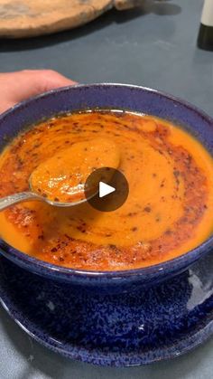 a bowl of soup with a spoon in it and someone's hand on the side