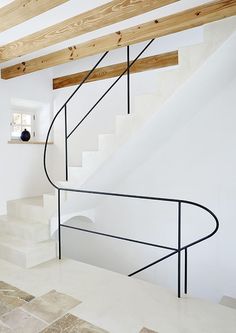 a white staircase with black handrails in a room that has wood beams on the ceiling