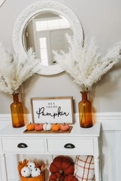 a white dresser topped with vases filled with pumpkins and cotton grass next to a mirror