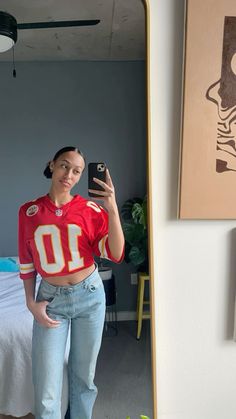 a woman taking a selfie with her cell phone in the mirror while wearing a football jersey