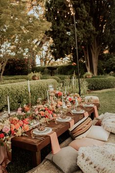 an outdoor table set up with flowers and candles for a dinner party in the garden