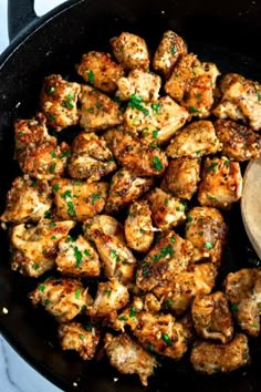 chicken in a skillet with a wooden spoon and parsley on the side, ready to be cooked