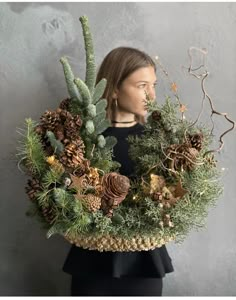 a woman holding a wreath with pine cones and evergreens