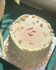 a white cake with pink decorations on it sitting on top of a table next to a basket