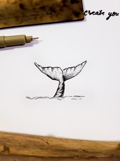 a drawing of a whale tail on top of a piece of paper next to a pen