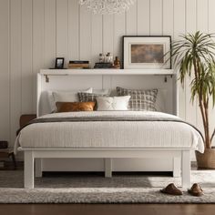 a white bed sitting in a bedroom next to a tall potted plant and a wooden floor