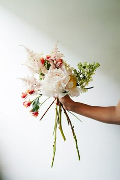 a person holding a bouquet of flowers in their hand with white wall and background behind them