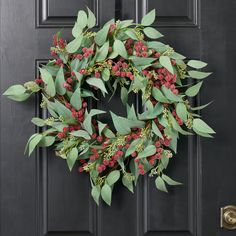 a wreath with red berries and green leaves hangs on the front door's black door