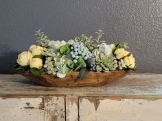 a wooden bowl with succulents and flowers in it sitting on a table