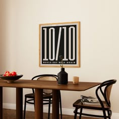 a dining room table with two chairs and a framed poster on the wall