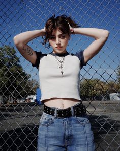 a young woman is posing in front of a fence with her hands on her head