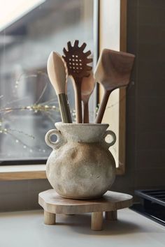 a vase with spoons and spatulas in it on a table next to a window