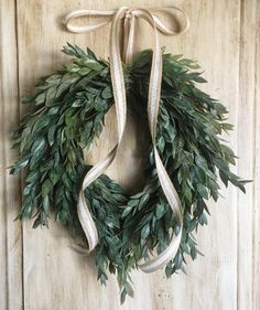 a wreath hanging on the wall with white ribbon and green leaves tied around it's edges