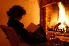 a woman sitting in a chair reading a book and holding a glass of red wine