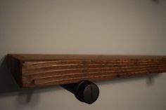 a wooden shelf with two black knobs mounted on it's sides and a white wall in the background